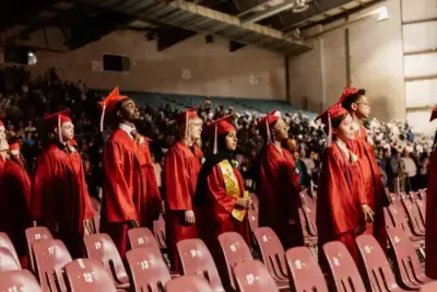 Graduates in red caps and gowns stand in a row at a ceremony, facing forward.