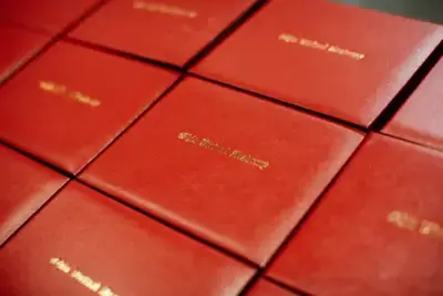 Red diploma covers embossed with gold lettering are neatly arranged in rows. The image exudes a sense of achievement and formality.